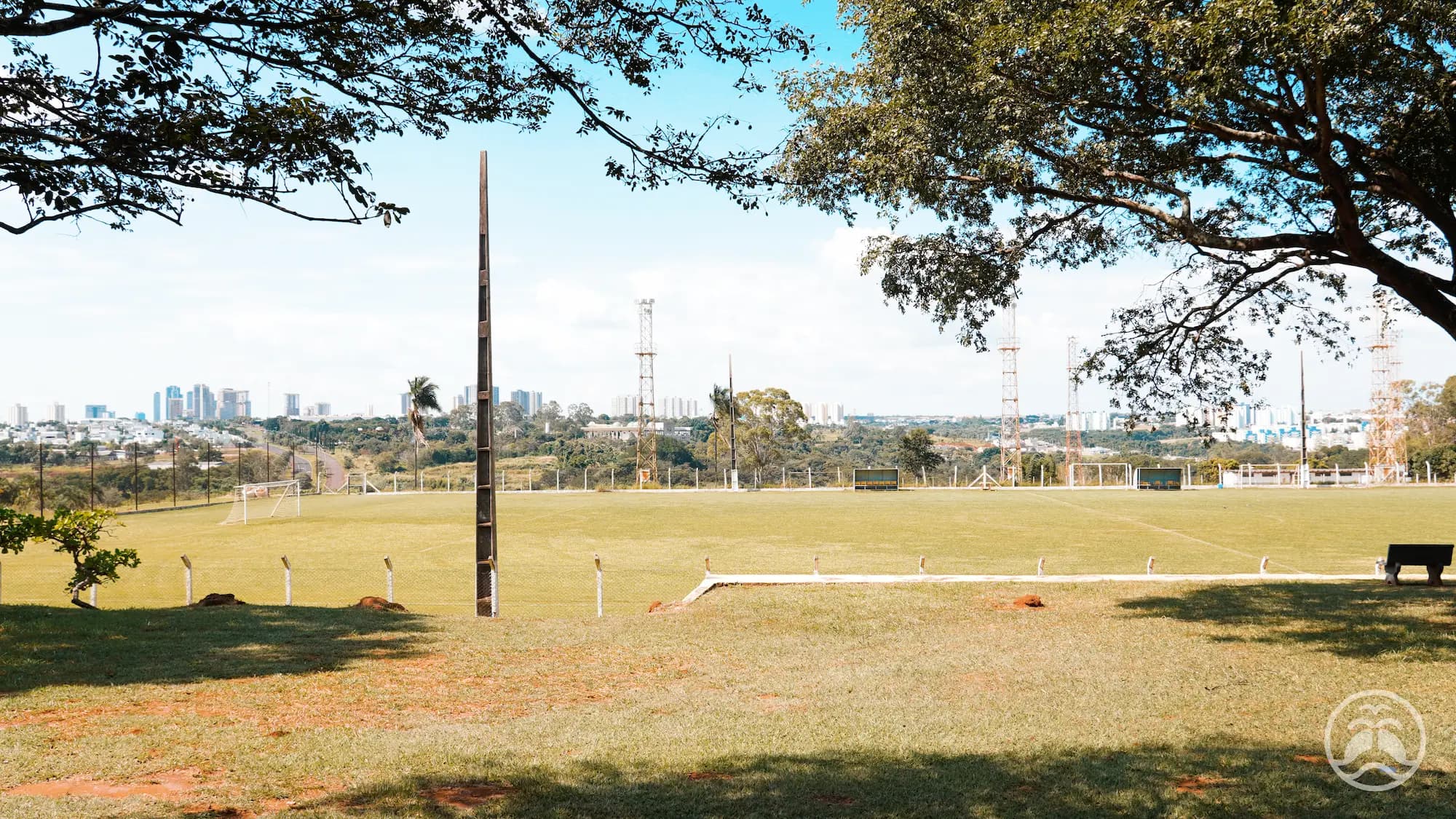 Campo de futebol do clube visto a partir de uma área sombreada com bancos e árvores.