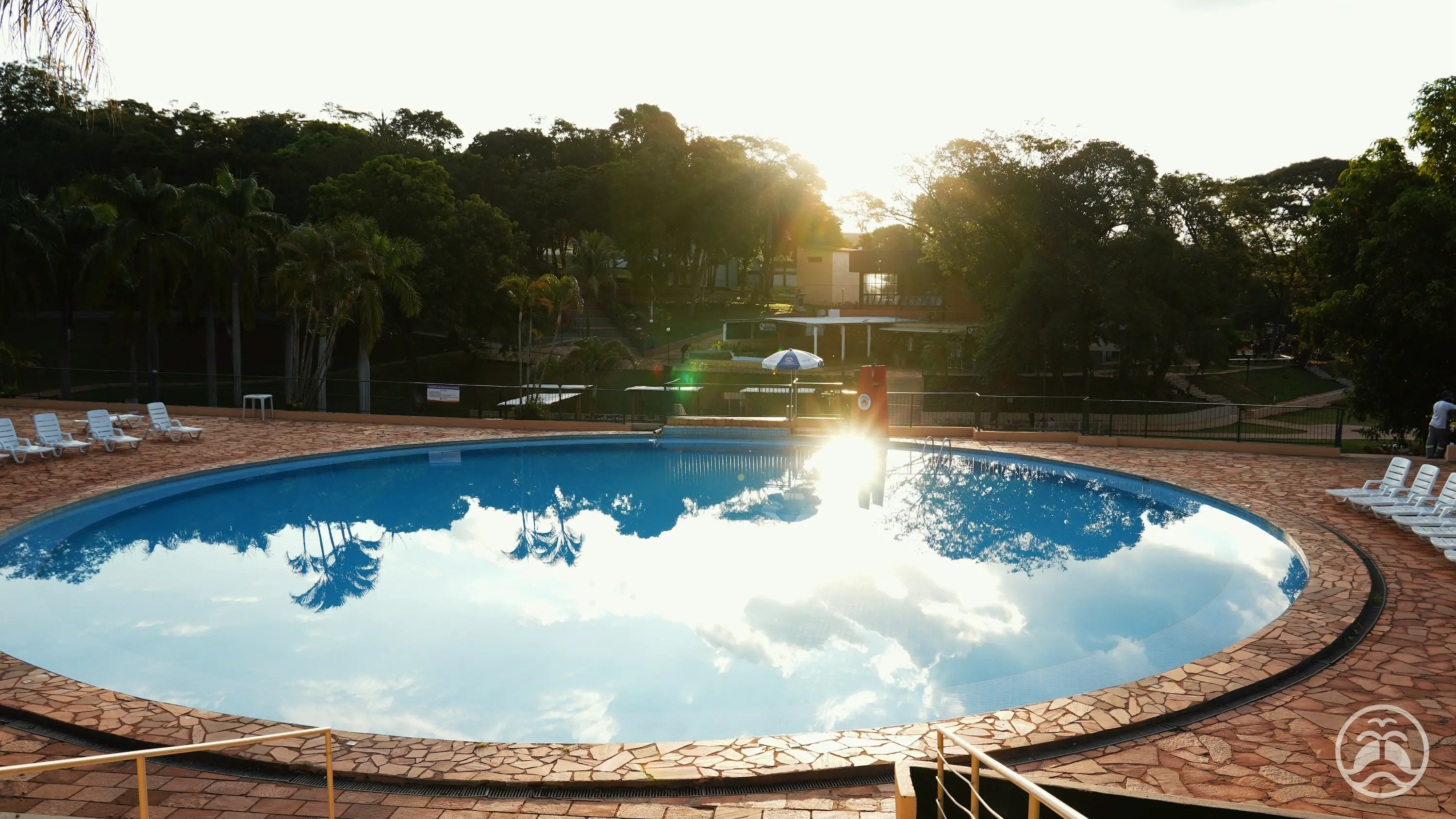 Piscina redonda refletindo o céu com a paisagem do clube ao fundo.